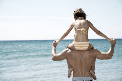 A father's love for his daughter: Girl (8-10) on father's shoulders by sea, rear view